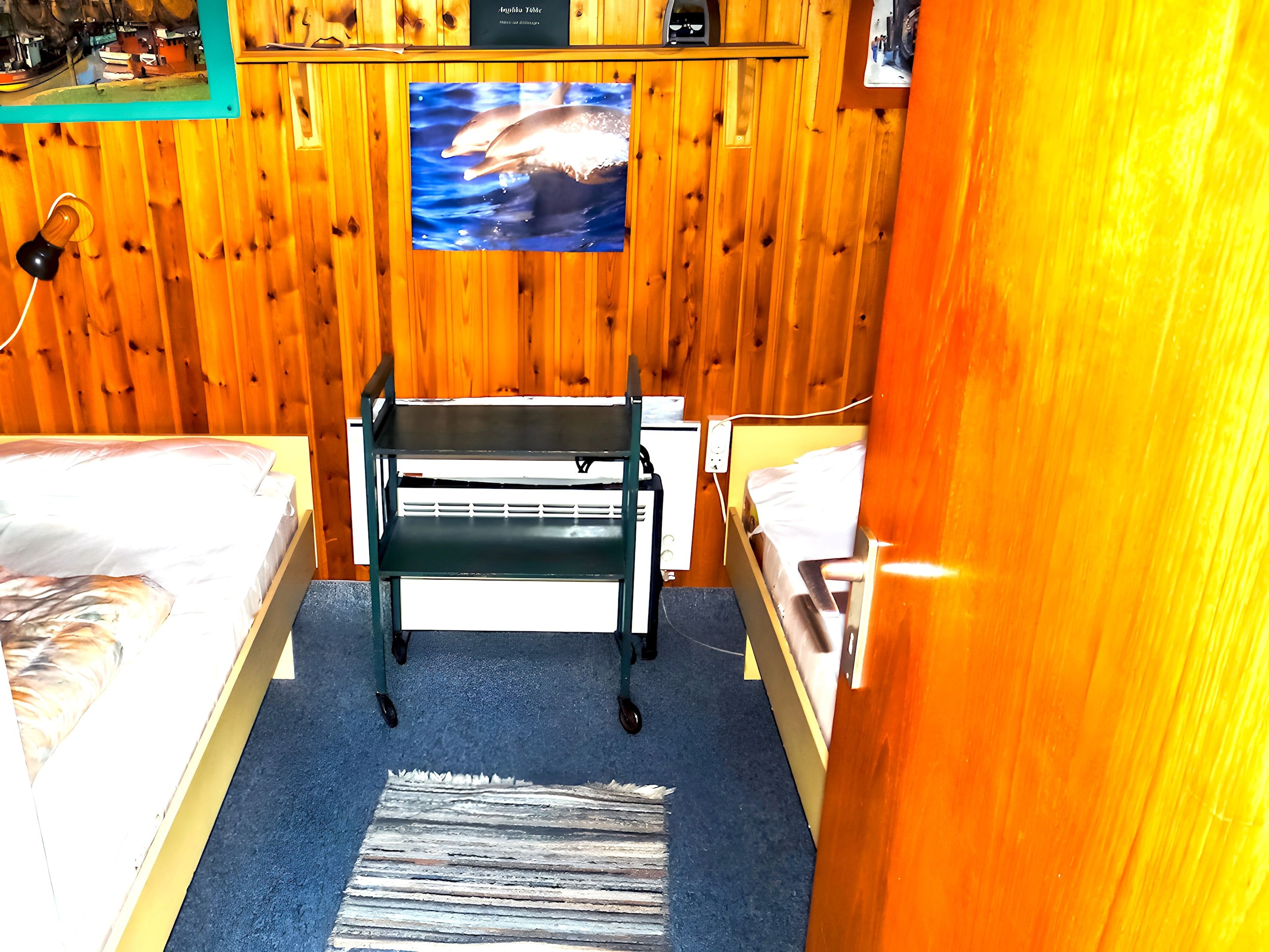 A small, cozy room with two beds, a desk, and a wooden wall.