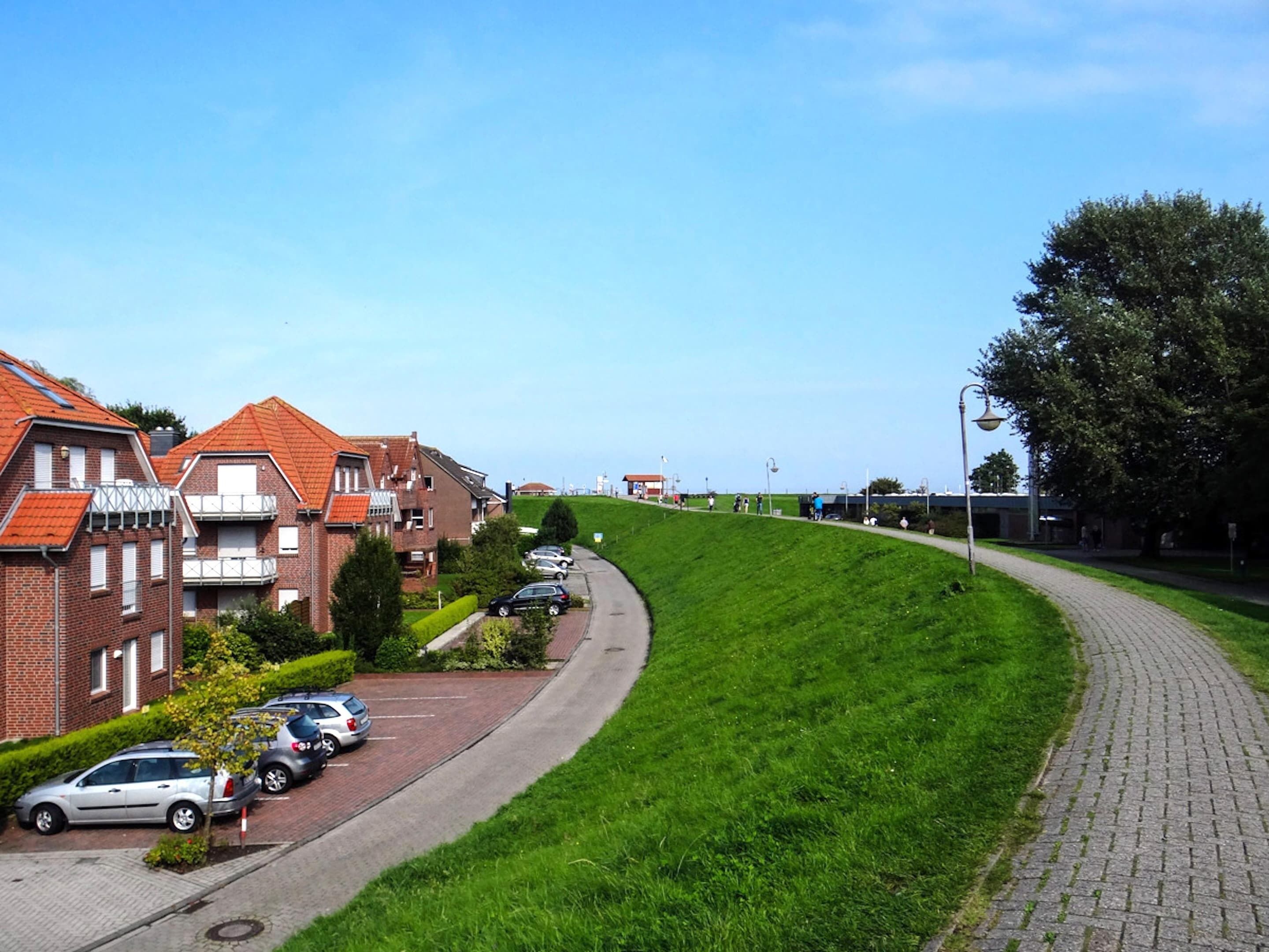 Een woonstraat met huizen, geparkeerde auto's en een grasheuvel.