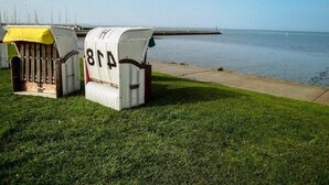 Two wicker chairs with numbers 814 and 815, placed on a grassy area near a body of water. - Nordsee-ferienhaus mit Terrasse (Wangerland)