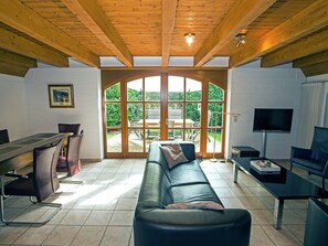 Relax in this open-plan living area with a high ceiling, featuring a large arched door to a garden view patio and a comfortable black leather sofa.