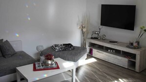 A modern living room with a grey sofa, a white coffee table with a decorative bowl, a wooden TV stand with a flat-screen TV, and a minimalist decor style. - Grosszugiger Komfort, Rubeland (Oberharz am Brocken)