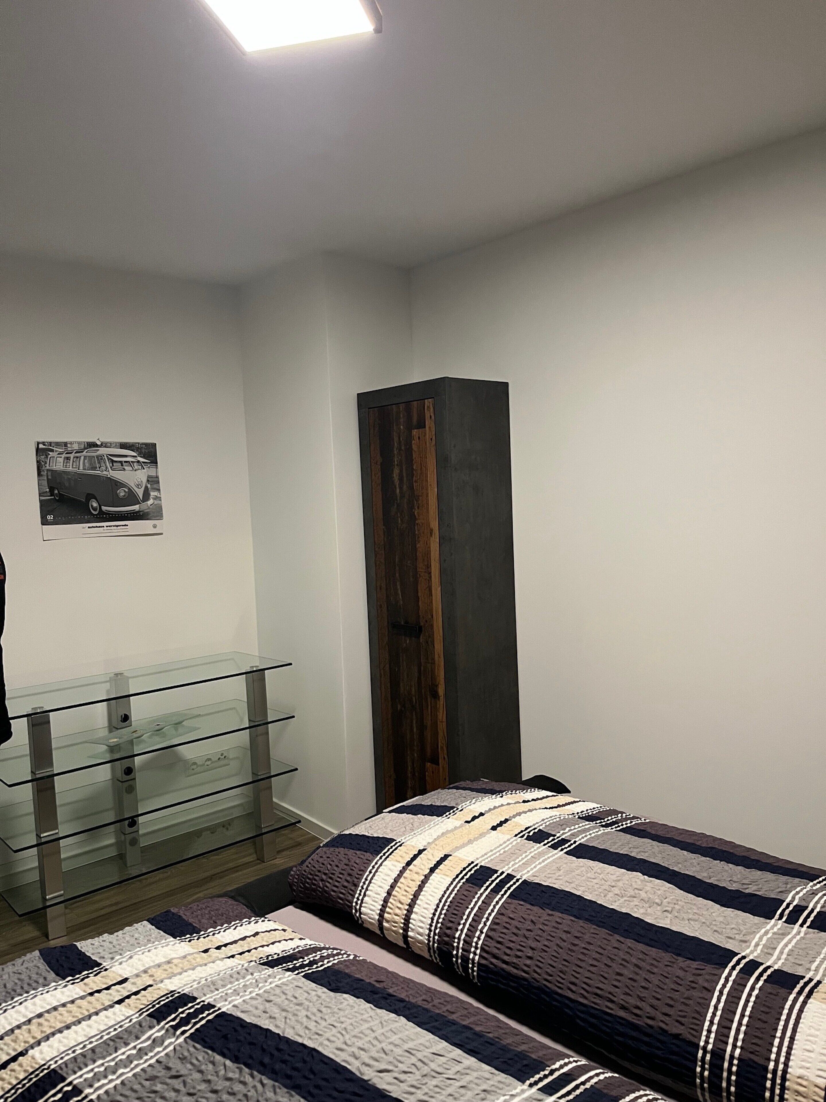 Un dormitorio con cama, cómoda de cristal, aparador de madera y un cuadro colgado en la pared.