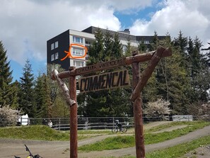 A wooden signpost with "DIKEPARK WINTERBERG COMMENCAL" written on it, set against a backdrop of a modern building and trees. - Apartment in Winterberg With Balcony (Winterberg)