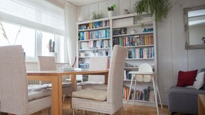 A modern living room with a wooden dining table, wicker chairs, a bookshelf filled with books, a grey sofa, and a large window with curtains. - Apartment in Winterberg With Balcony (Winterberg)