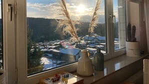 A window with a view of a snowy landscape and a village, a vase, and a small table with a chessboard. - Apartment in Winterberg With Balcony (Winterberg)