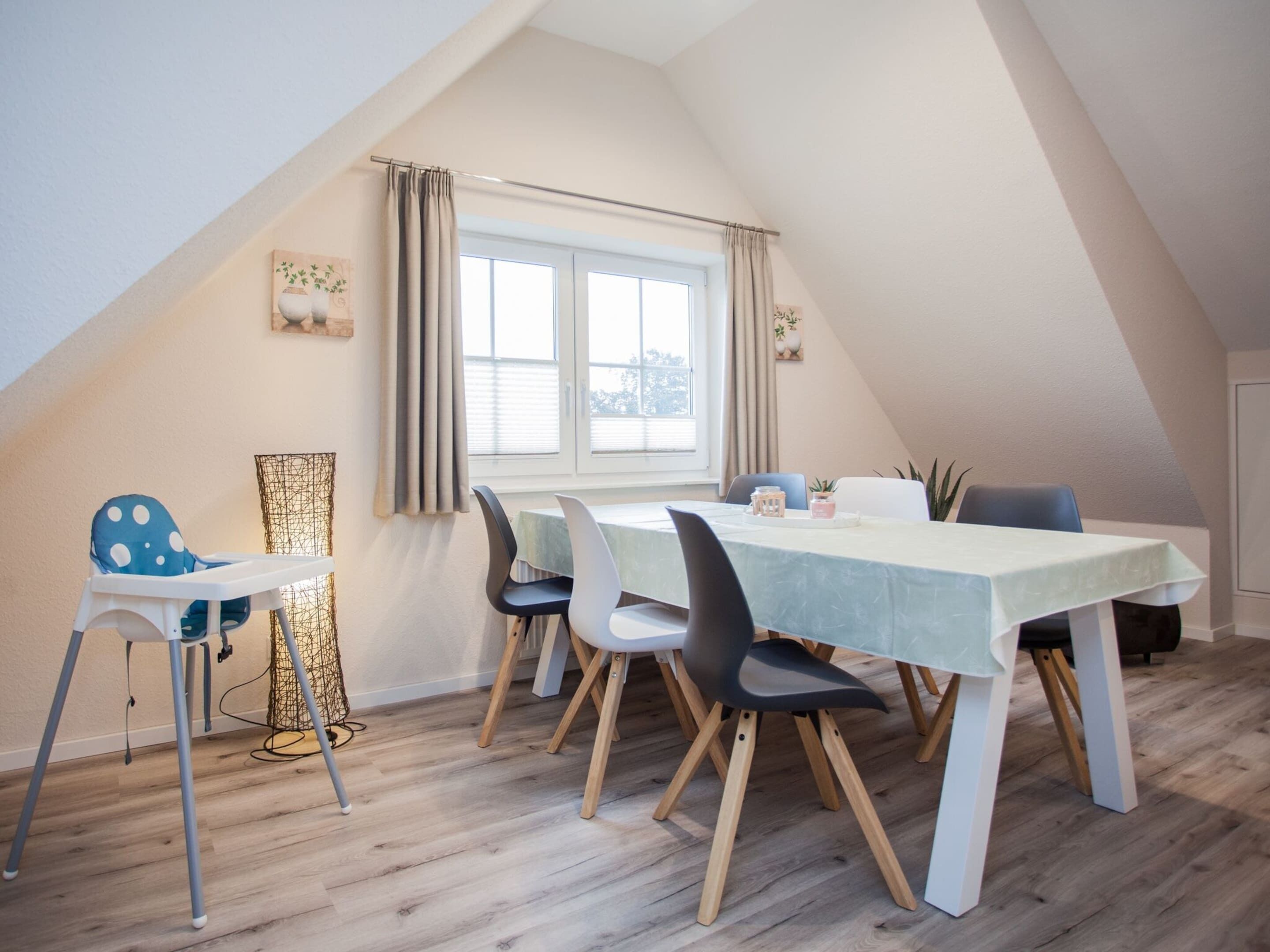 Ein Essbereich mit Tisch und Stühlen, einer hohen Decke und einem mit Vorhängen drapierten Fenster.