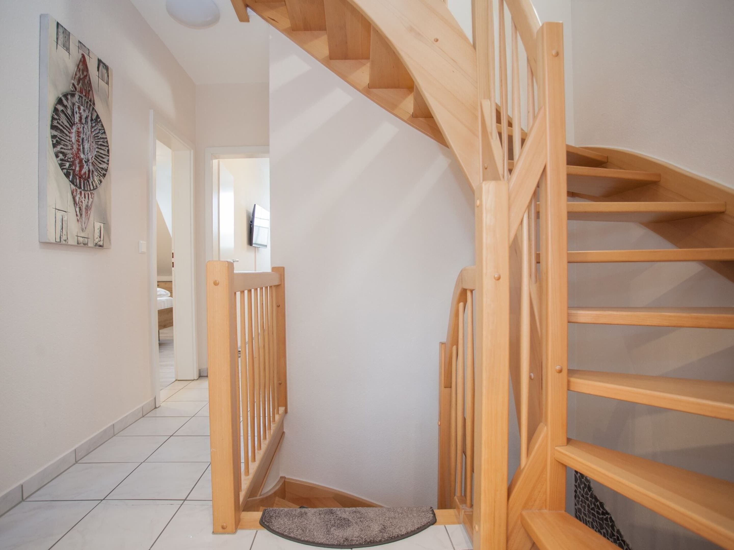 A wooden staircase with a handrail, leading to a landing with a door and a small rug.