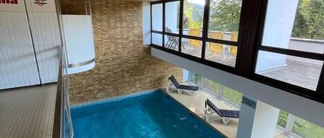 An indoor swimming pool with clear windows, a brick wall, and lounge chairs.