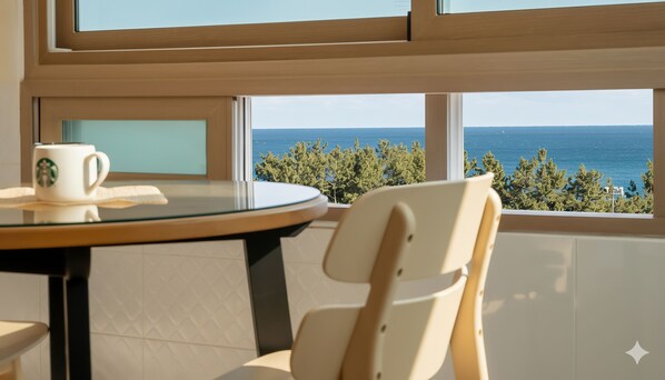 A room with a round table, a white chair, and a view of the sea through large windows. - Sokcho Pensionbyeol (Sokcho)