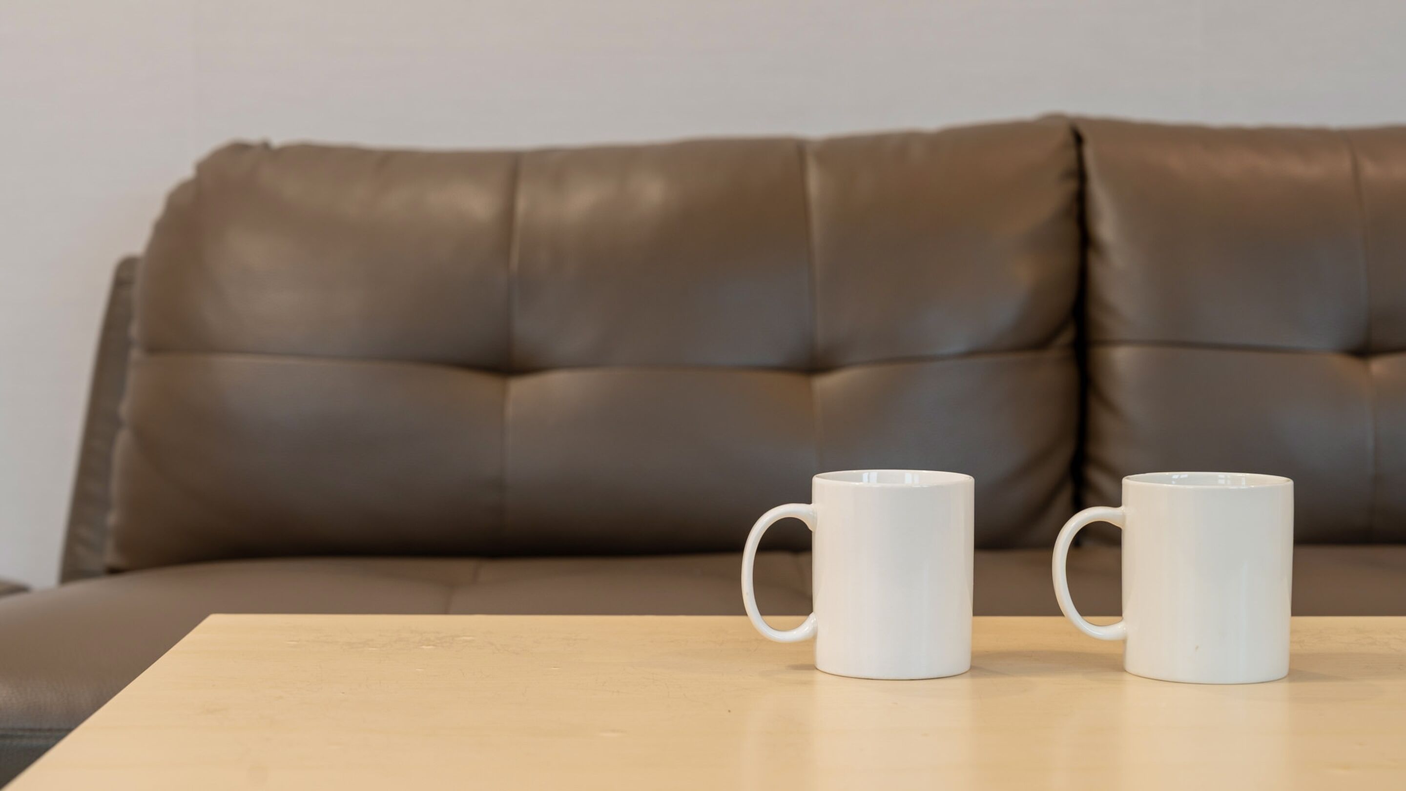A brown leather sofa with two white mugs on a wooden table.