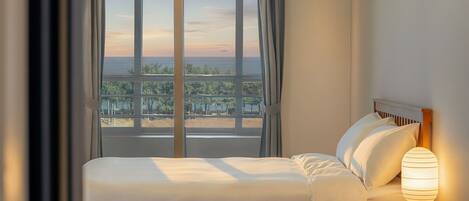 A hotel room with a large window, a bed with white linens, and a bedside lamp.