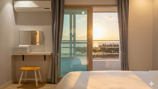 A hotel room with a bed, a small stool, a shelf with a mirror, and a view of a bridge and sunset. - Sokcho Pensionbyeol (Sokcho)