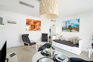 Een moderne woonkamer met een bank, stoelen, een eettafel gedekt voor twee personen, en kunstwerken aan de wanden.