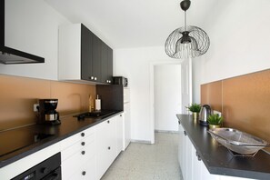 A modern kitchen with a black countertop, white cabinets, a coffee machine, and a unique pendant light. - Vacation Home "Sun Club Maspalomas" with Pool, Tennis Court & Wi-Fi (Maspalomas)