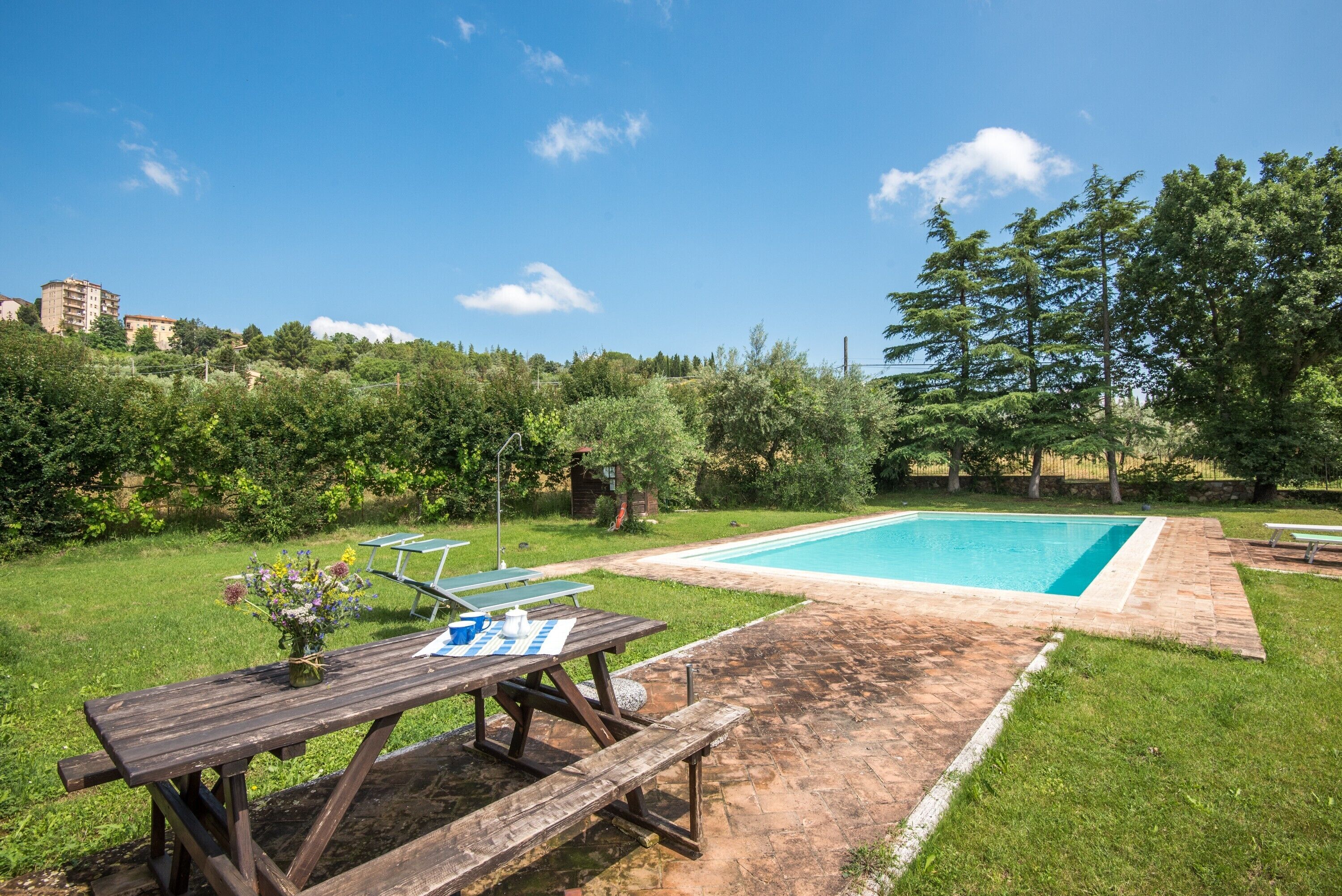 Un jardin avec une piscine, une table de pique-nique en bois et une pelouse.