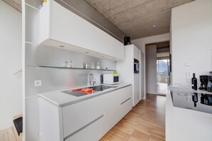 A modern kitchen with white cabinetry, a glass shelf, a microwave, and a sink.