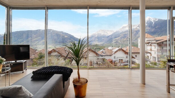 A modern living room with a large window, a flat-screen TV, a sofa, and a potted plant. - Apartment 'Villa Alvarium Eins' with Mountain View, Private Terrace and Wi-Fi (Scena)