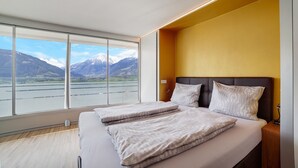 A modern hotel room with a large window, a bed with two pillows, and a bedside table. - Apartment 'Villa Alvarium Eins' with Mountain View, Private Terrace and Wi-Fi (Scena)