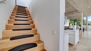 A modern staircase with wooden steps and black non-slip runners, leading to a bright kitchen area with white cabinetry and a view of greenery outside. - Apartment 'Villa Alvarium Eins' with Mountain View, Private Terrace and Wi-Fi (Scena)