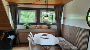 A cozy room with a wooden ceiling, a white table with chairs, a bench, and two windows with curtains.