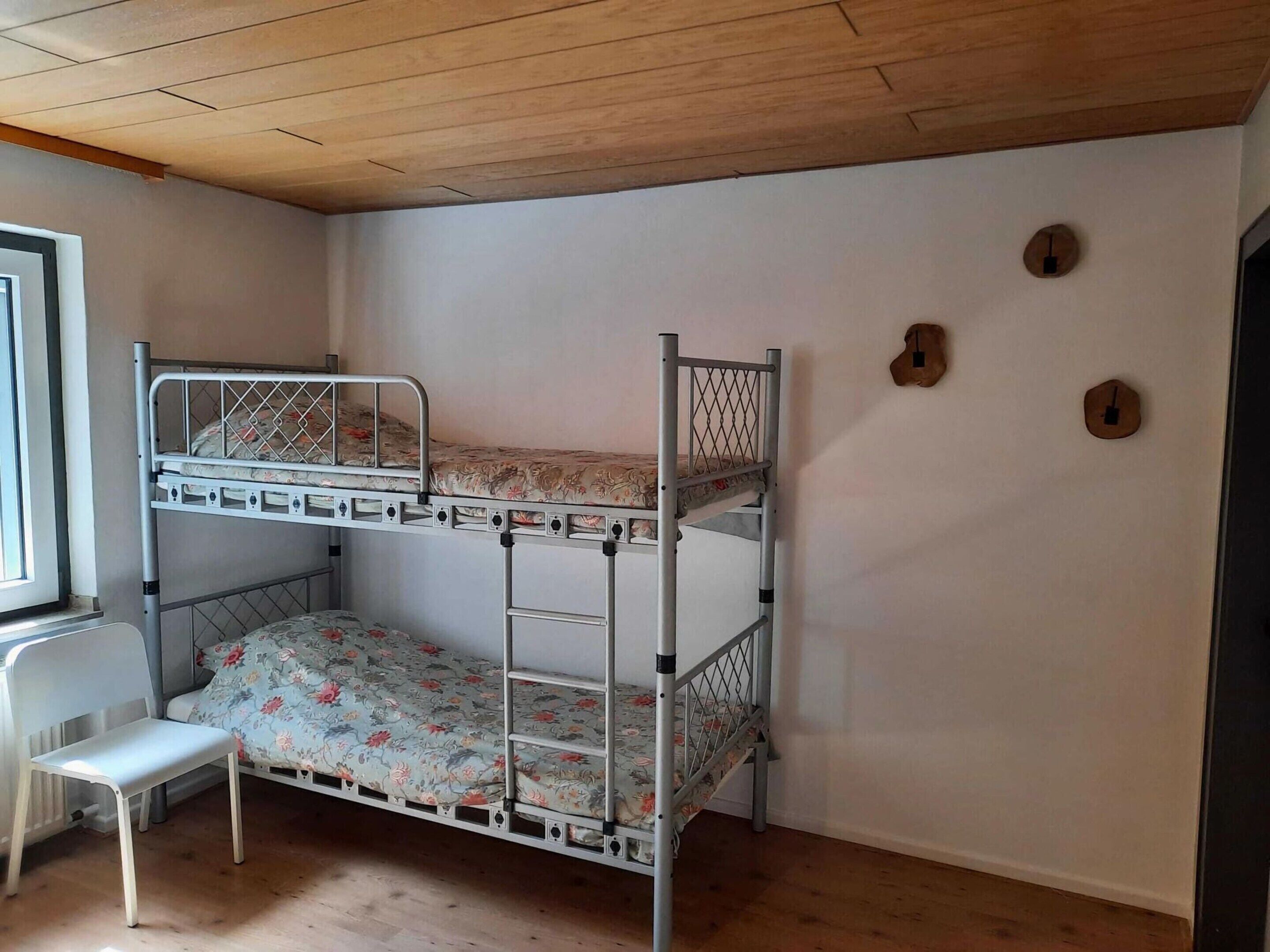 Et soveværelse med køjeseng, hvid stol og et vindue.