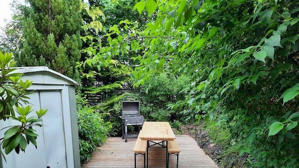 A wooden deck with a picnic table and grill, surrounded by lush greenery.
