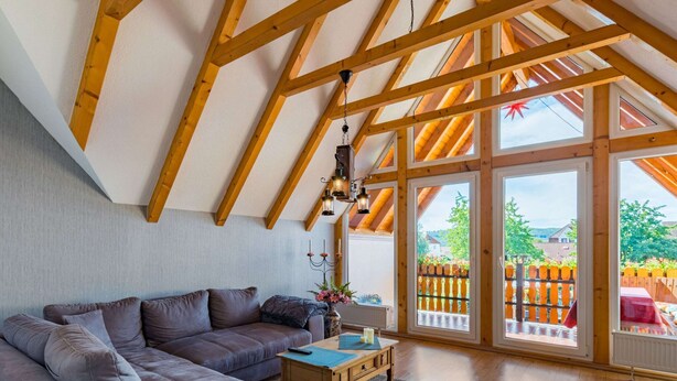 Un salon moderne avec un plafond en bois, un canapé gris, une table basse en bois et de grandes fenêtres donnant sur un jardin.