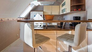 Une cuisine compacte dotée d’un îlot central, de deux tabourets de bar et d’une étagère en bois agrémentée d’objets décoratifs.