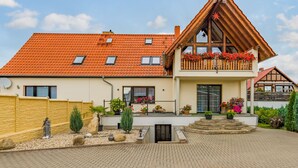Une maison à deux étages avec un toit recouvert de tuiles rouges, un balcon orné de jardinières et une allée pavée.