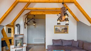 Un salon chaleureux avec une cheminée, des poutres en bois, un canapé et un tableau.