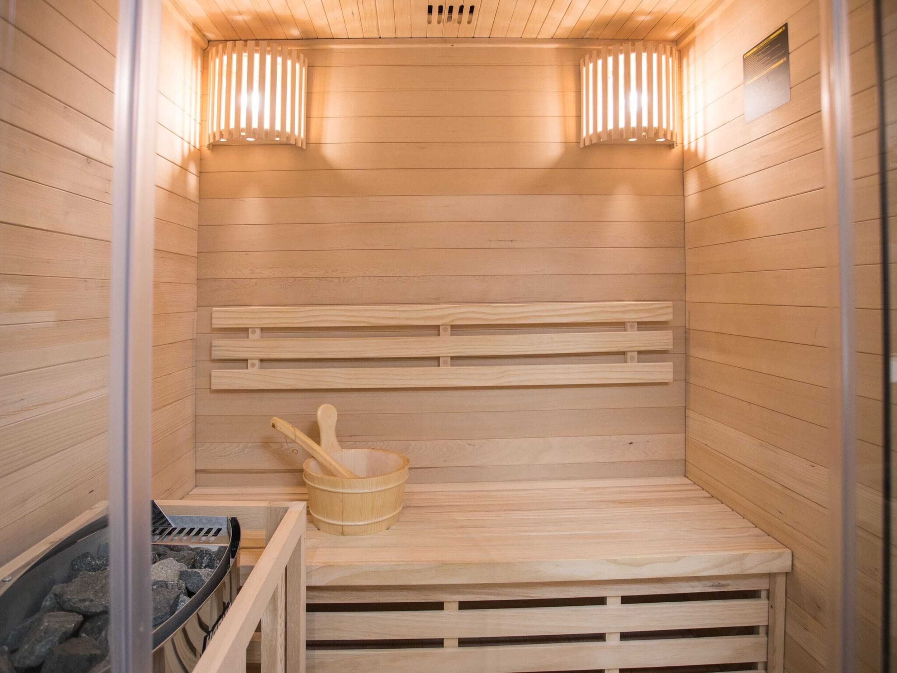A sauna with wooden benches, a wooden bucket, and a stone-filled container.