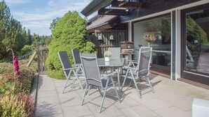 An outdoor patio with a table and chairs, a grill, and a view of the surrounding garden and trees. - Modern Ferienhaus Nahe von Winterberg mit Garten (Winterberg)