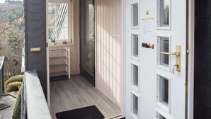 A wooden exterior door with a small window, a metal handrail, and a black mat at the entrance. - Modern Ferienhaus Nahe von Winterberg mit Garten (Winterberg)
