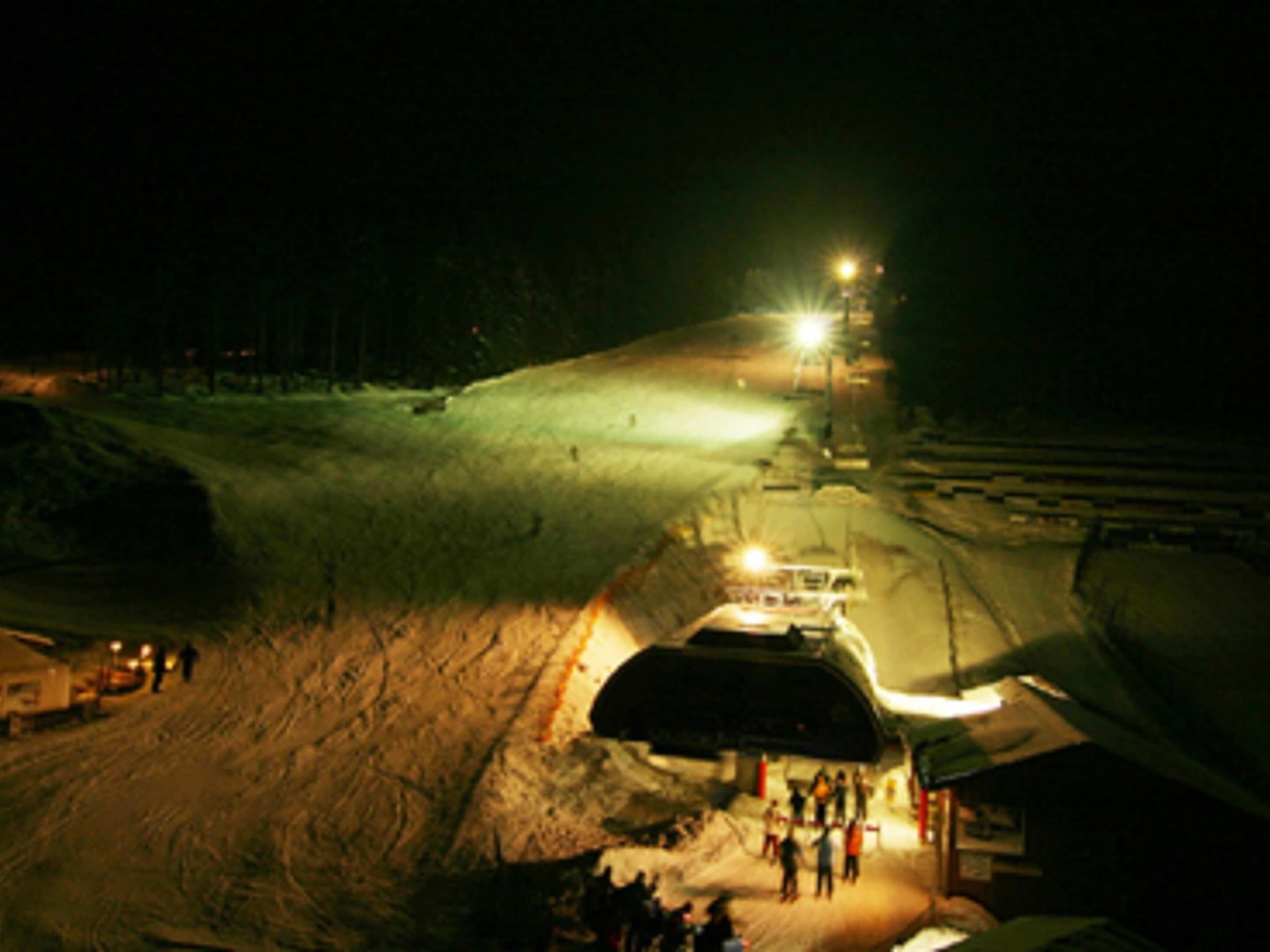 A snow-covered slope with a tunnel entrance, a vehicle, and people gathered at the tunnel's opening.