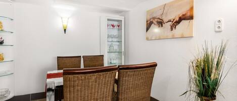 A dining area with wicker chairs, a glass table, and a painting on the wall.