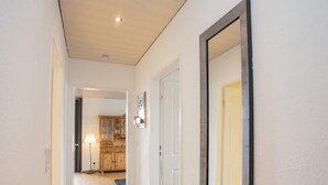 A hallway with a wooden floor, white walls, and a large mirror on the right. There is a door on the left and a cabinet in the background. - Wohnung in Winterberg mit Balkon in Pistennahe (Winterberg)