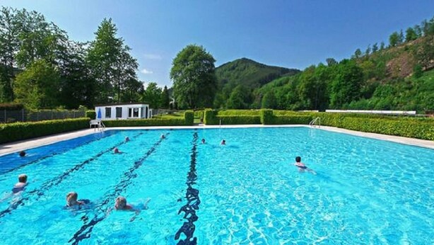 A swimming pool with clear blue water, surrounded by greenery and hills. - Wohnung in Winterberg mit Balkon in Pistennahe (Winterberg)