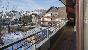 A balcony with a view of a snowy residential area, including houses and parked cars. - Wohnung in Winterberg mit Balkon in Pistennahe (Winterberg)
