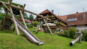 Ein Spielplatz mit Rutsche und Schaukeln in einer grünen Wiese, im Hintergrund Häuser.