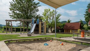 Ein Spielplatz mit Rutsche und Klettergerüsten, umgeben von einem Sandkasten und Picknicktischen.