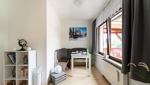 Un salon moderne avec une bibliothèque blanche, un canapé gris, une table à manger et une fenêtre avec des rideaux.