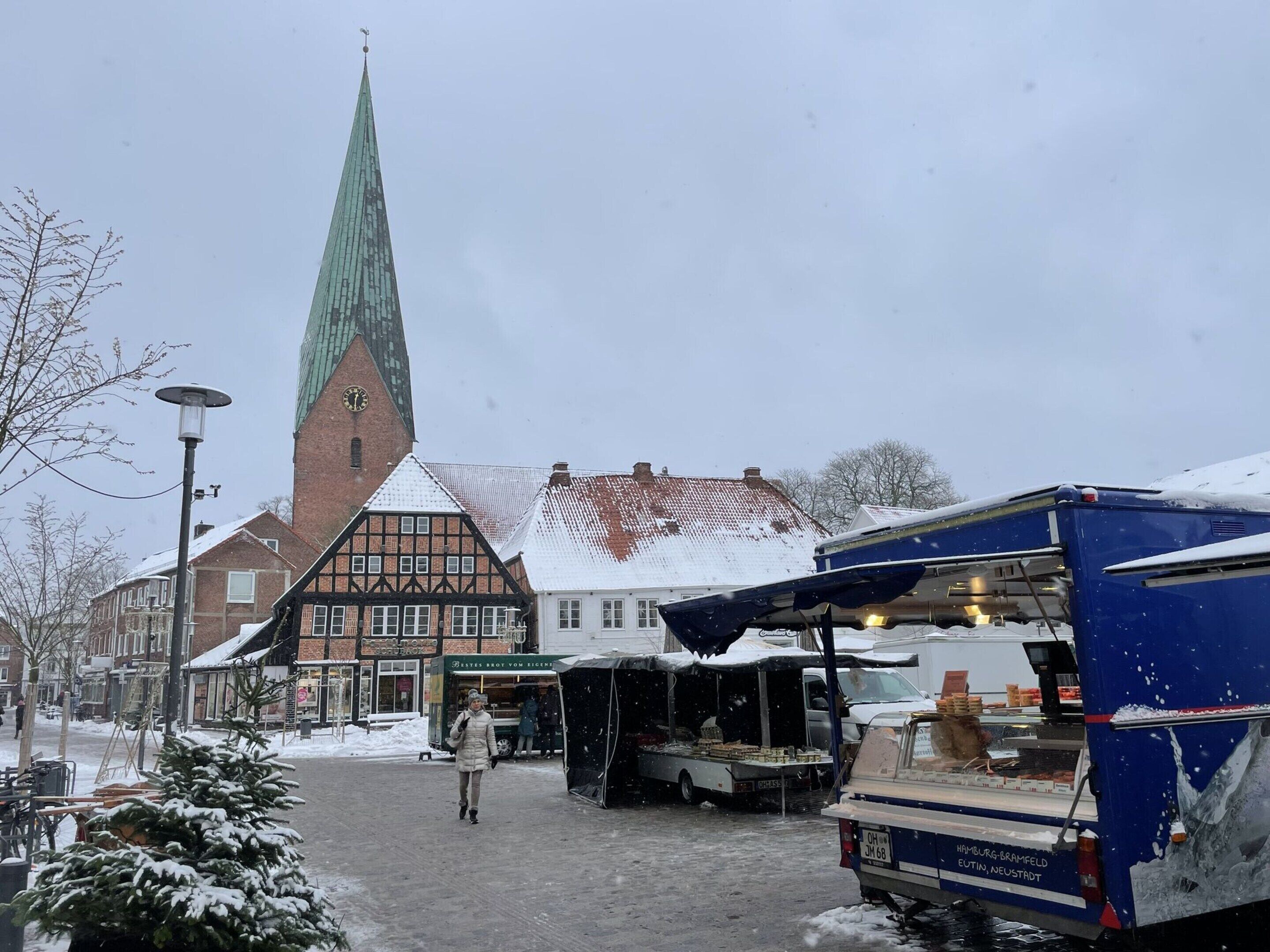 A snow-covered street with a church, a market stall, and a blue truck.
