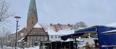 A snow-covered street with a church, a market stall, and a blue truck.