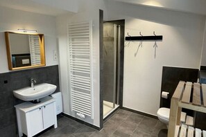 A modern bathroom with a white sink, a glass shower enclosure, and a wooden vanity. - Wilma Holiday Home Directly at the Baltic Sea (Zierow)