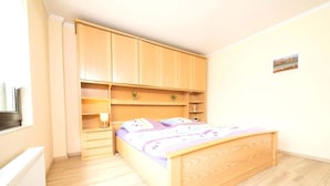 A bedroom with a wooden bed, built-in shelving, a bedside table, and a radiator. - Apartment on a Farm Near Dusseldorf (Juechen)