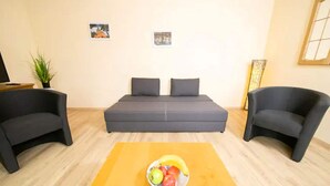 A modern living room with a sofa bed, two armchairs, a wooden coffee table with fruit, and a potted plant. - Apartment on a Farm Near Dusseldorf (Juechen)