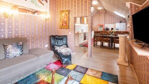 Uma sala de estar com sofá, uma poltrona preta, um tapete colorido e um canto de jantar com mesa e cadeiras.