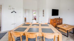 A modern, well-lit room with a wooden dining table, chairs, a TV, and a wooden cabinet. - Ferienwohnung Eifelruhe in Filz (Filz)