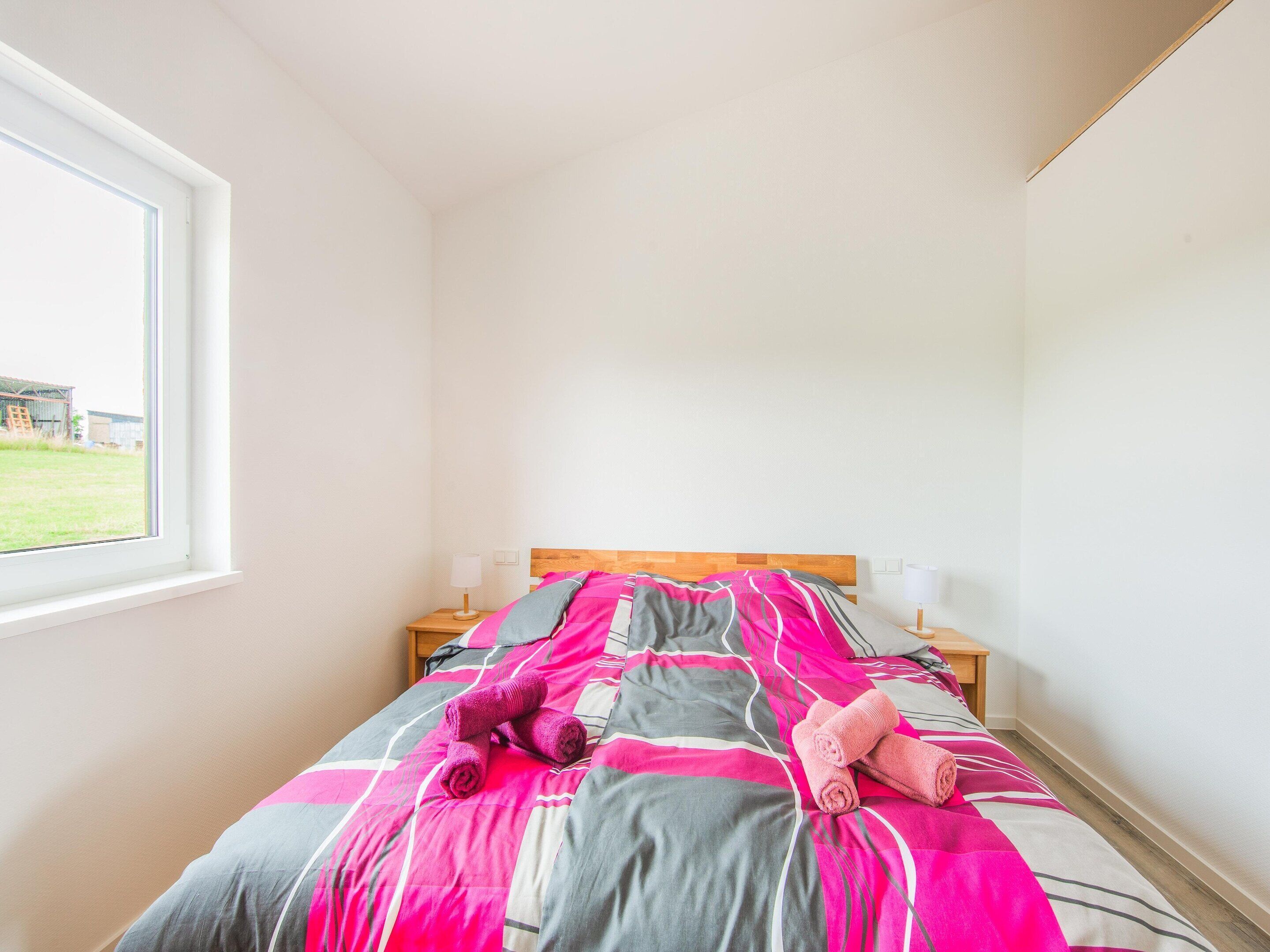 A single bed with a wooden headboard, two bedside tables with lamps, and a window with a view of a building and grass.