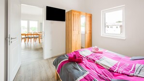 A bedroom with a bed, a wooden wardrobe, a TV mounted on the wall, and a window. - Ferienwohnung Eifelruhe in Filz (Filz)